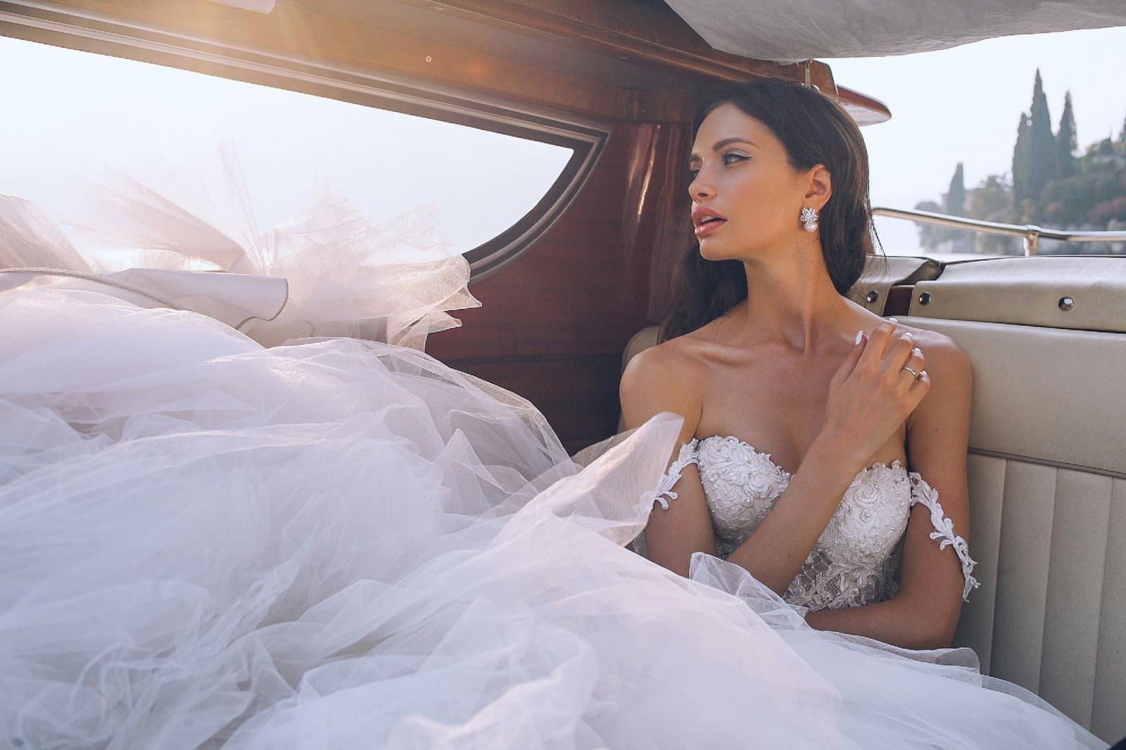 A bride in an elegant gown looking out over the water at sunset.