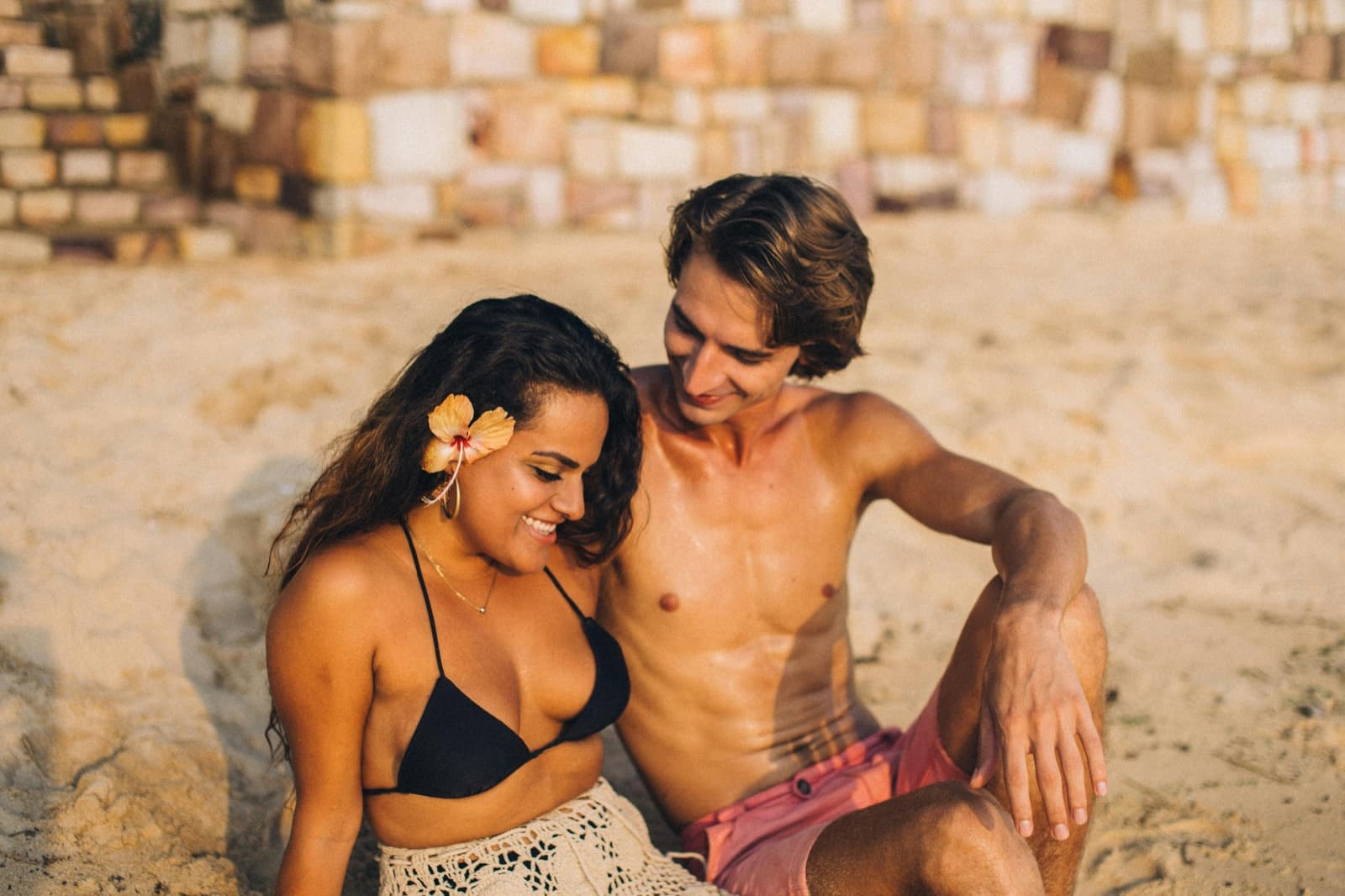 A couple sitting together on the sand at golden hour, relaxed and happy.