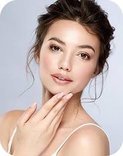 A woman in her 30s with fresh, glowing skin, hand raised gently to her face.